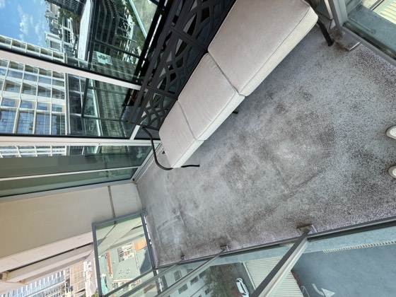 Balcony before cleaning &mdash; grey mottled staining across the floor, seat cushions still in place.